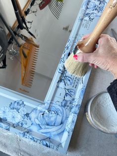 a person using a brush to paint a flower design on a mirror with blue flowers