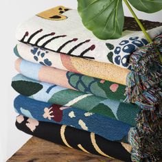 a stack of colorful towels sitting on top of a wooden table next to a potted plant