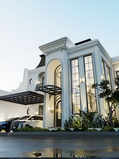 a large white building with lots of windows and plants in the front yard, next to a parking lot