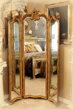 an ornately decorated gold mirror stands in front of a bed and chandelier