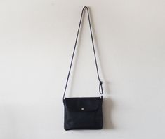 "This small crossbody bag features soft black leather with fabric lining, an adjustable shoulder strap, and a magnetic closure. Details: -Dimensions: 7\" length (top to bottom), 8\" bottom width (side to side), 3\" depth, 8\" X 3\" base (bottom) -Shoulder strap measures approx. 45-50\" total (adjustable) -Navy interior lining -Internal pocket -Magnetic closure Because each bag is made by hand, the measurement is approximate and may vary slightly from one bag to another. Options: #1 Vegan (fake) Black Crossbody Flap Bag With Adjustable Strap, Black Crossbody Shoulder Bag With Magnetic Closure, Black Leather Satchel With Fold Over Clasp, Black Flap Bag For Everyday Use, Black Flap Bag With Adjustable Strap For Everyday, Black Flap Shoulder Bag With Fold Over Clasp, Black Shoulder Flap Bag With Fold Over Clasp, Black Soft Leather Crossbody Flap Bag, Black Flap Bag With Adjustable Strap