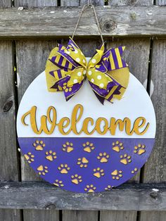 a purple and yellow welcome sign hanging from a wooden fence with paw prints on it