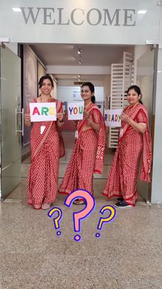 three women standing in front of a welcome sign with question marks on the floor next to them