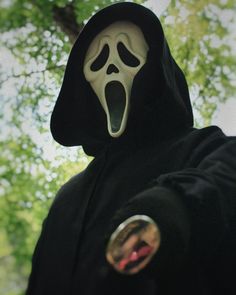 a person wearing a black hooded jacket with a ghost face on it