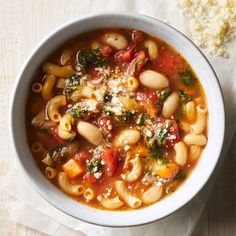 a white bowl filled with pasta and vegetables on top of a table next to a piece of bread