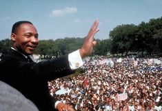 a man giving a speech in front of a large crowd with his hands up to the sky