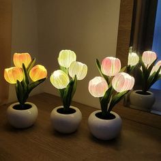 three white vases filled with flowers on top of a wooden table next to a mirror