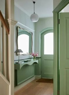 a hallway with green walls and wooden flooring next to a mirror on the wall