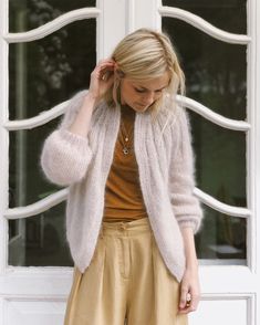 a woman standing in front of a window with her hand on her head and looking down