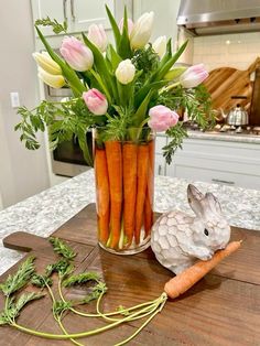 a vase filled with carrots and flowers on top of a wooden table next to a bunny statue