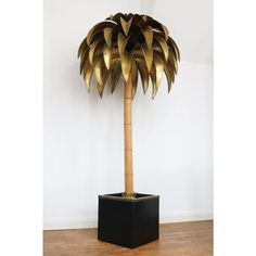 a palm tree made out of gold leafy branches in a black planter on a wooden floor