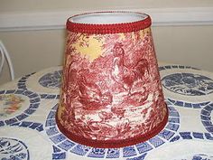 a red lamp shade sitting on top of a blue and white tablecloth covered table