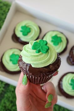 a person holding up a cupcake with green frosting and shamrock decorations on it