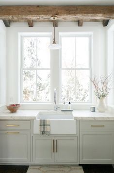 a kitchen with white cabinets and counter tops next to a window that has wooden beams