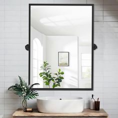 a white sink sitting under a large mirror next to a potted plant on top of a wooden table