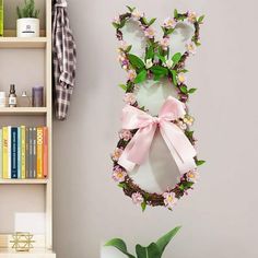 a bunny shaped wreath hangs on the wall next to a potted plant and bookshelf