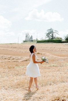 a woman in a white dress is standing in a field holding a bouquet of flowers