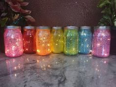 there are many different colored jars with lights in them on the marble counter top next to potted plants