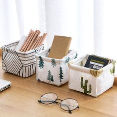 three storage containers with books, pencils and glasses on a wooden table next to a laptop