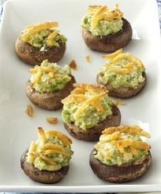 a white plate topped with stuffed mushrooms covered in guacamole and cheddar