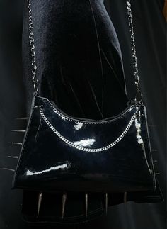 "This sharp goth PVC baguette purse is lined with silver metal spikes and features a gorgeous dangling stainless steel cuban chain on each side. The perfect accessory for any alternative, punk, or goth baddie out there! The long PU Leather chain allows this to be worn as a crossbody or on the shoulder.  SIZE: The bag length measures approximately 9.6\", the bag width is approximately 2.8\", and the height is approximately 6.7\".  The handle adds approximately 25\" so that this can be worn on the shoulder or as a crossbody.  MATERIAL/FEATURES: Has a total of 15 40MM metal spikes, 4 12MM spikes, and 2 stainless steel cuban chains. The purse itself is made of 100% PVC leather on the outside and 100% PU leather on the inside. The chain is iron linking with PU Leather and attached to two stainl Baguette Purse, Goth Baddie, Cuban Chains, Metal Spikes, Faux Leather Purse, Gothic Punk, Cuban Chain, Leather Chain, Steel Chain