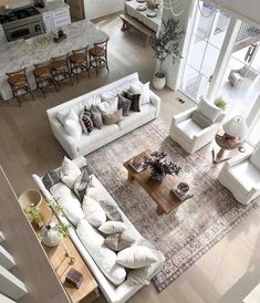 an aerial view of a living room with white furniture and large windows overlooking the kitchen