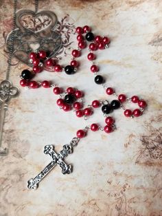 This set of prayer beads is made with red and black glass pearls and features a silver-toned budded crucifix. This rosary is hand-wired using stainless steel eye pins and my trusty little looper tool. The beads are connected by these loops. The smaller beads are 8mm red glass pearls. The larger beads are 10mm black glass pearls. The focal point is a silver-toned budded crucifix. It measures 56x34mm. 25.4mm is about 1 inch. The cross is silver-toned metal. The jump rings are aluminum. This rosary Handmade Red Rosary With Cross, Handmade Red Cross Rosary, Handmade Red Rosary, Types Of Prayer, Chakra Colors, Beads Charms, Eye Pins, Inexpensive Gift, Chakra Healing