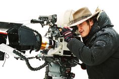 a man with a hat on holding a camera in front of a snow covered field