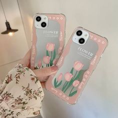 two iphone cases with flowers on them in front of a white wall and light fixture