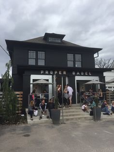 people are sitting on the steps in front of a black building with white doors and windows