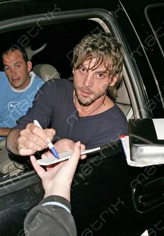 the man is sitting in the car signing autographs for someone else to sign up