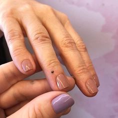 two hands with manicured nails holding each other's fingers and one has a small black dot on the tip