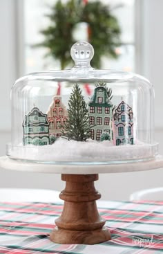 a glass covered cake plate on top of a table with a christmas tree in it