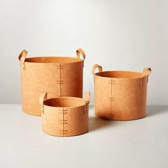 three brown leather buckets with handles on white surface