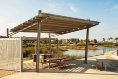 a covered picnic area next to a body of water with benches and tables under it