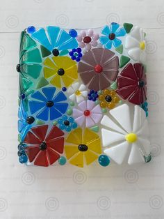 a multicolored glass tile with flowers and beads on the bottom is mounted on a white wall