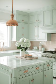 a kitchen with green cabinets and white flowers in a vase on the island countertop