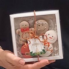 a person holding a box filled with christmas cookies in it's hands and an ornament hanging from the front