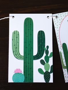 two cards with cactus designs on them sitting next to each other in front of a wooden table