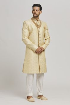 Ivory and golden sherwani with floral frame embroidery. Paired with an inner kurta and churidar. - Aza Fashions Gold Jamawar Sets For Reception, Traditional Gold Raw Silk Wear With Naqshi, Gold Traditional Wear With Naqshi Drape, Gold Jamawar Kurta With Resham Embroidery, Gold Raw Silk Sherwani With Zari Work, Festive Gold Sherwani With Naqshi Detailing, Festive Gold Sherwani With Naqshi, Ceremonial Beige Zari Work Sherwani, Ceremonial Beige Sherwani With Zari Work