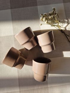 four cups sitting on top of a table next to a vase with flowers in it