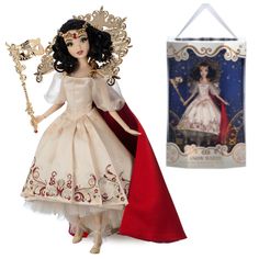 a doll with a red cape and white dress is next to a box that has a gold crown on it