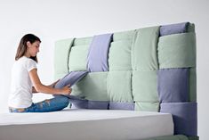 a woman sitting on top of a bed next to a white wall and holding pillows