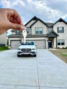 a hand holding a key to a white car parked in front of a large house