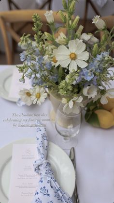 a table set with blue and white flowers in a vase on top of a plate