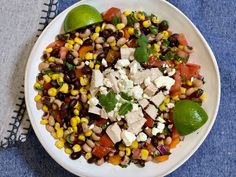 a white bowl filled with corn, black beans and feta cheese on top of a blue table cloth