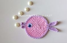 a crocheted pink fish with blue eyes on it's back and white pearls around its neck