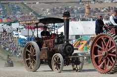 an old fashioned tractor being driven by two men in the middle of a dirt field