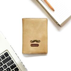 a leather wallet with a mustache on it next to a laptop computer and notepad