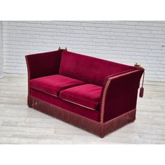 a red couch sitting on top of a wooden floor next to a white brick wall